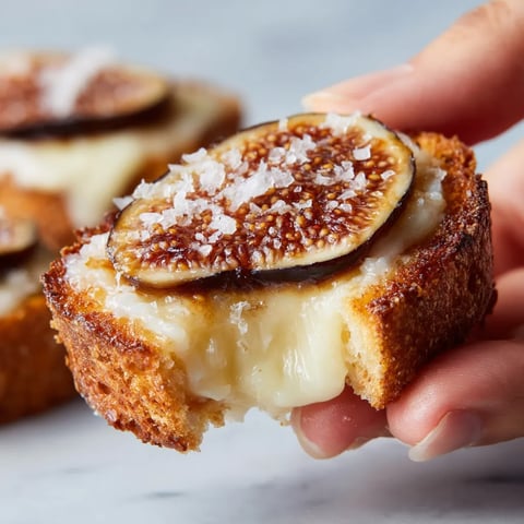 Una mano sostiene un trozo de pan tostado con manchego y figas.