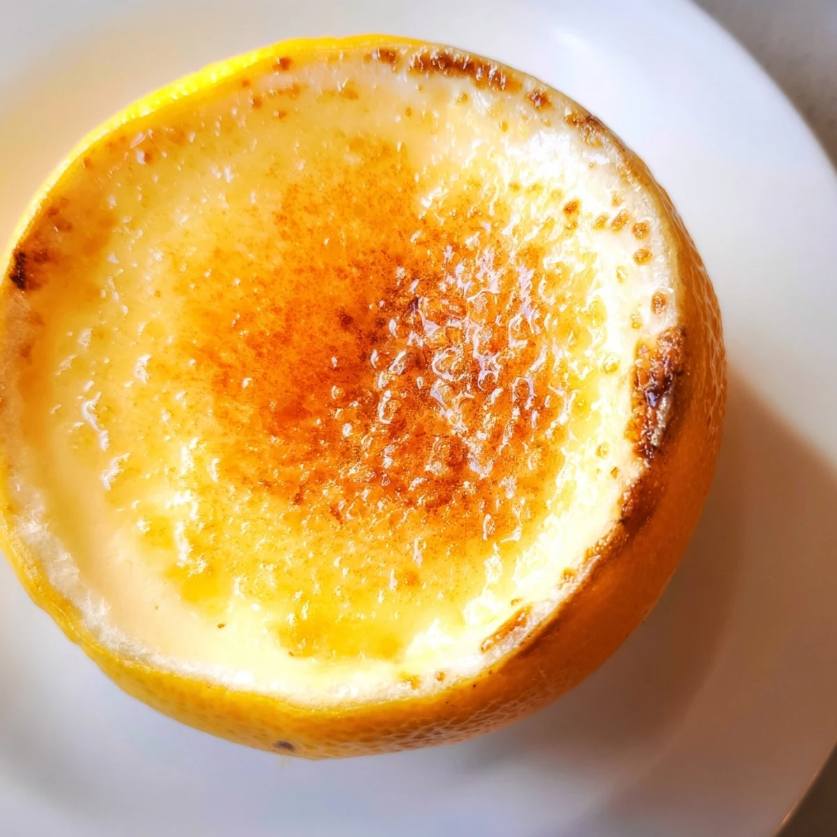 Creamy, rich Lemon Brûlée Posset dessert, served inside bright yellow lemon shells, caramelized topping.
