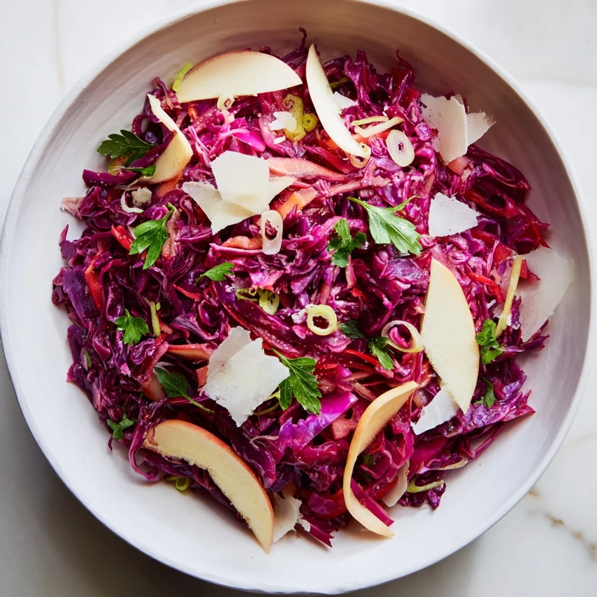 Cruda col lombarda roja brillante con tiras de manzana y virutas de queso parmesano, espolvoreada con perejil fresco.