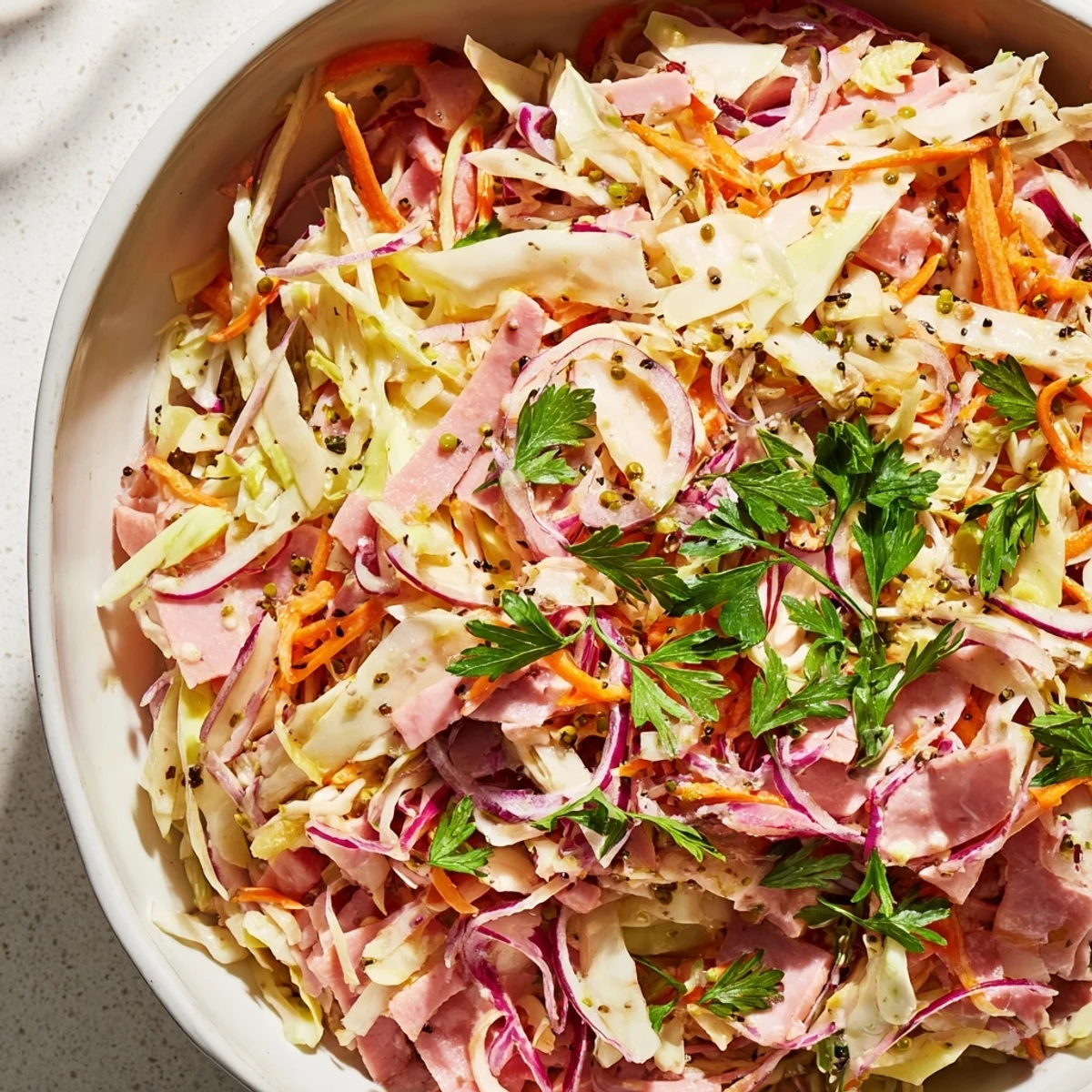 Un bol grande de German Cabbage Coleslaw With Shredded Ham, con repollo crujiente, zanahoria y jamón ahumado brillante.