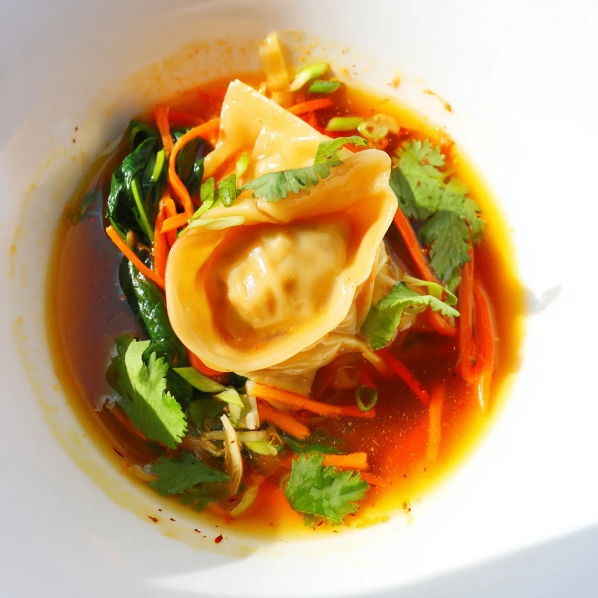 Una tazón de Red Curry Wonton Soup con espinacas baby y zanahorias ralladas en un caldo cremoso y especiado.