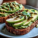2. Creamy mashed avocado spread on toasted whole grain bread with crisp green apple slices and nutty pumpkin seeds for added crunch.