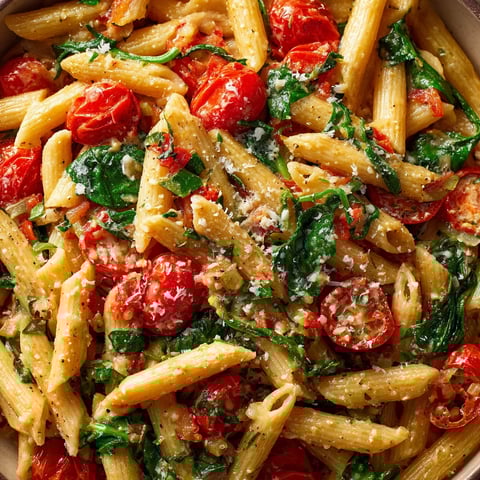 Un plato de pasta con tomates y espinacas.