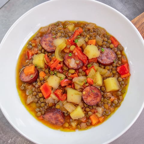 Tazon humeante de estofado de lentejas y chorizo, un plato español rústico con verduras.