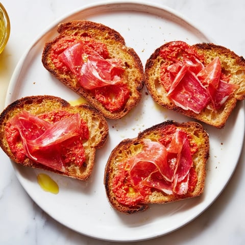 Crispy pan con tomate, topped with jamón, drizzled with olive oil, ready to eat.