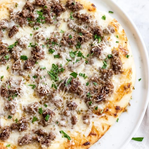 Ground Beef Alfredo Pizza, a cheesy delight, features a bubbling mozzarella topping and rich Alfredo sauce.