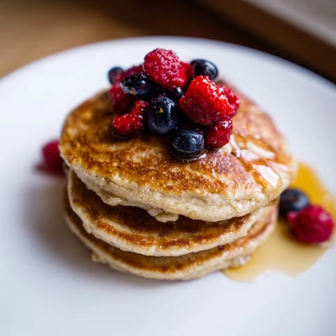 Fluffy brown banana pancakes, golden and ready, served with fresh berries and syrup.