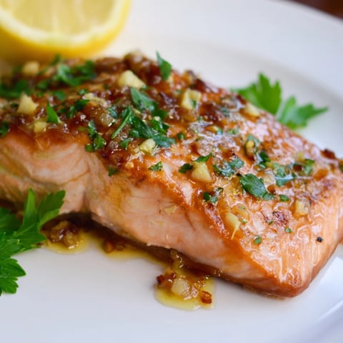 Juicy honey garlic glazed salmon, glistening on a plate, ready to be served with lemon wedges.
