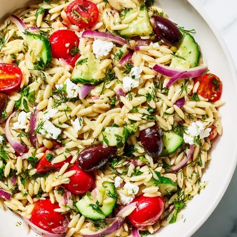 A vibrant image shows the prepared Greek Orzo Salad with fresh vegetables and creamy feta.