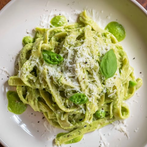 Creamy Green Pea Alfredo pasta is blanketed in a vibrant, smooth sauce, sprinkled with herbs.