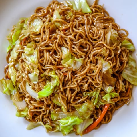 Un plato de Fried Cabbage Ramen con fideos dorados y repollo crujiente en un wok