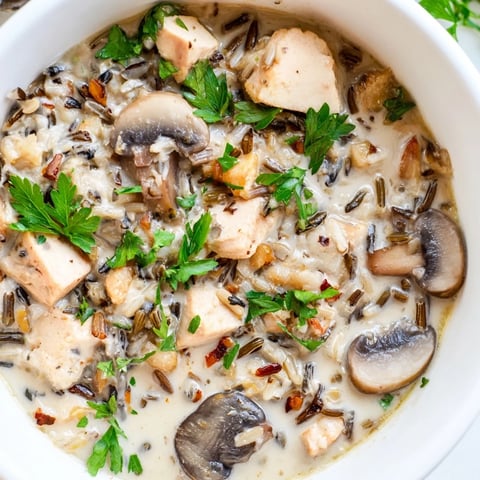 Una cuchara grande de sopa cremosa de pollo, champiñones y arroz salvaje, servida en un tazón para una cena reconfortante.