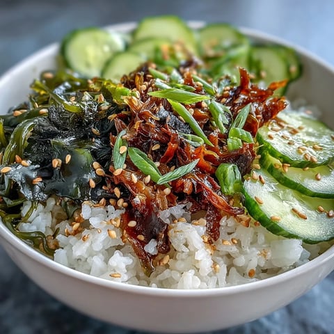 Bowl de arroz con nori y algas sobre arroz blanco, con rodajas de pepino y semillas de sésamo tostado.