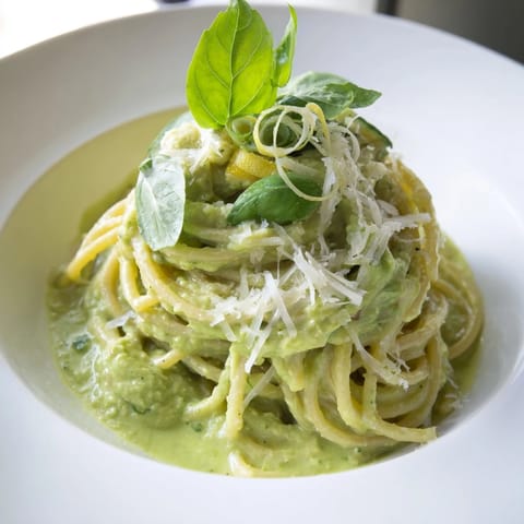 Freshly made creamy avocado pasta, garnished with basil and parmesan, ready to savor.