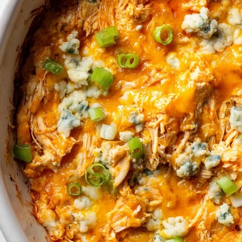 Vista cenital de Buffalo Chicken Dip recién horneado, burbujeante y dorado con cebollino fresco y alitas de pollo tiradas.