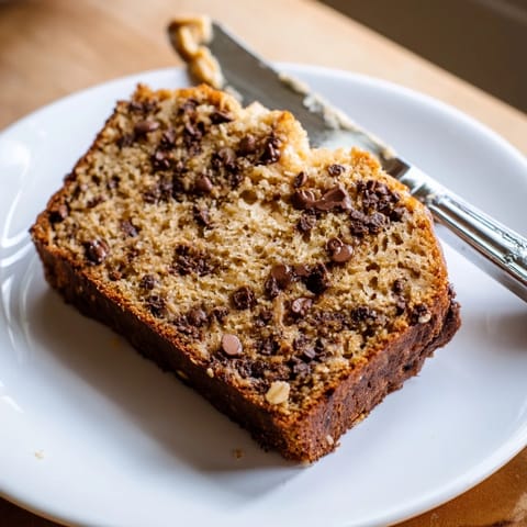 Pan de plátano avena mantequilla de maní y chips de chocolate con trozos de plátano maduro y nueces, en rebanada sobre tabla de cortar.