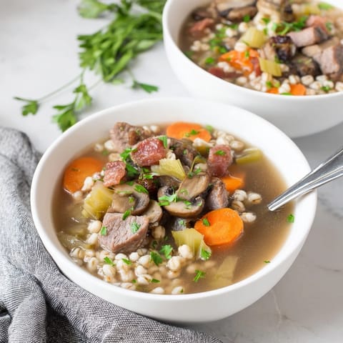 Un bol humeante de Sopa de Res y Cebada con Champiñones, con trozos tiernos de carne y garnitura de perejil fresco.