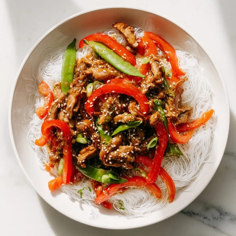 A close-up of a steaming bowl of Mongolian Chicken with Rice Noodles, savory and delicious.