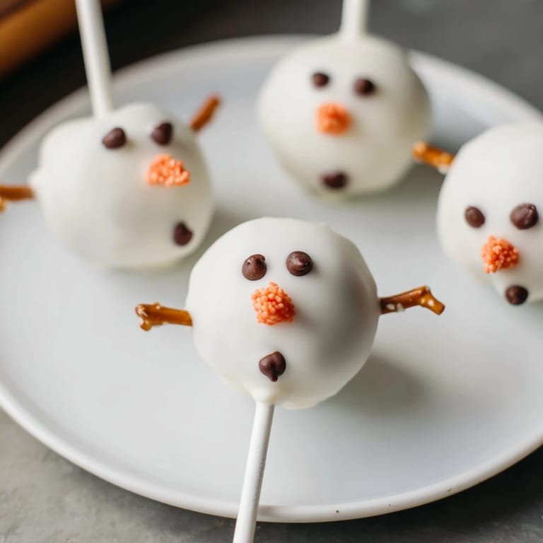 Close-up of freshly dipped Oreo Snowman Cake Pops, showcasing playful shapes and vibrant chocolate decorations.
