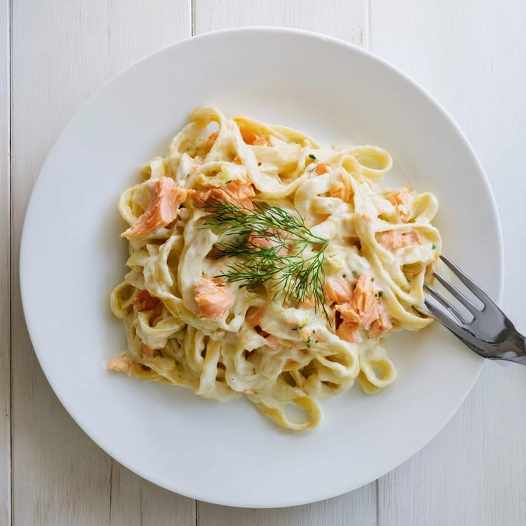 Salmón ahumado y pasta fettuccine en salsa cremosa, servida con hierbas frescas y limón.